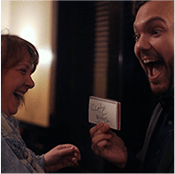A man, corporate mentalist, holds a card while a woman laughs.